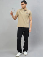 Man wearing 98degreenorth Men's Beige Aero Club No.3 Polo T-Shirt, black pants, white sneakers, holding sunglasses.