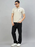 Man in 98degreenorth Men's Beige Polo T-Shirt, black jeans, white sneakers, and sunglasses stands against a gray backdrop.