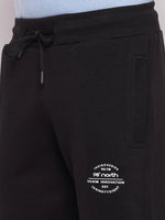 A close-up of a person wearing 98degreenorth Men’s Black Fleece Trackpants with a drawstring and white text near the pocket.