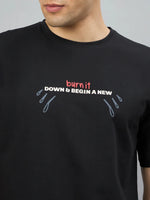 A man wears a 98degreenorth black oversized tee with "Burn It Down" and blue teardrop graphics on the sides.