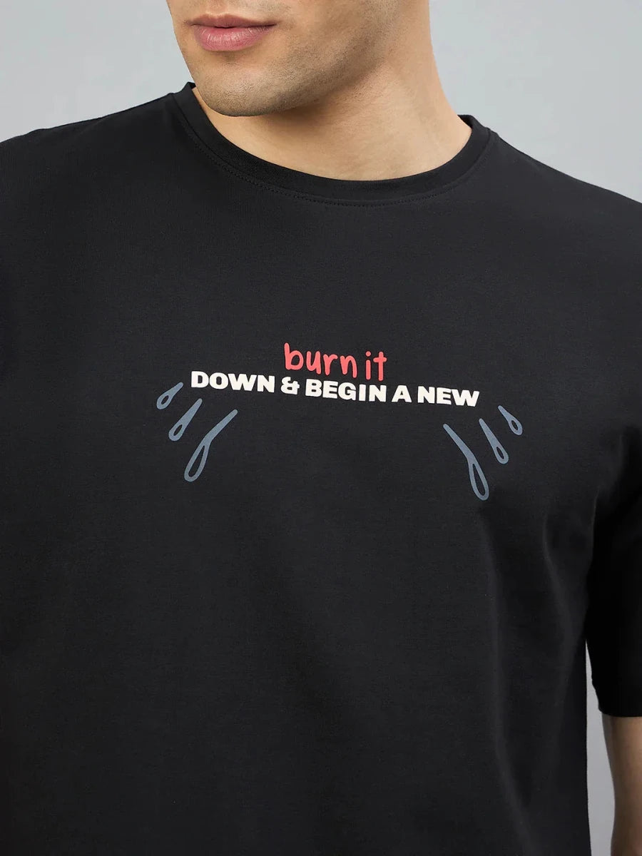 A man wears a 98degreenorth black oversized tee with "Burn It Down" and blue teardrop graphics on the sides.