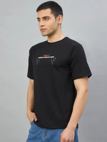 Young man in a 98degreenorth Men's Black Graphic Oversized T-Shirt, standing sideways with hands in pockets.