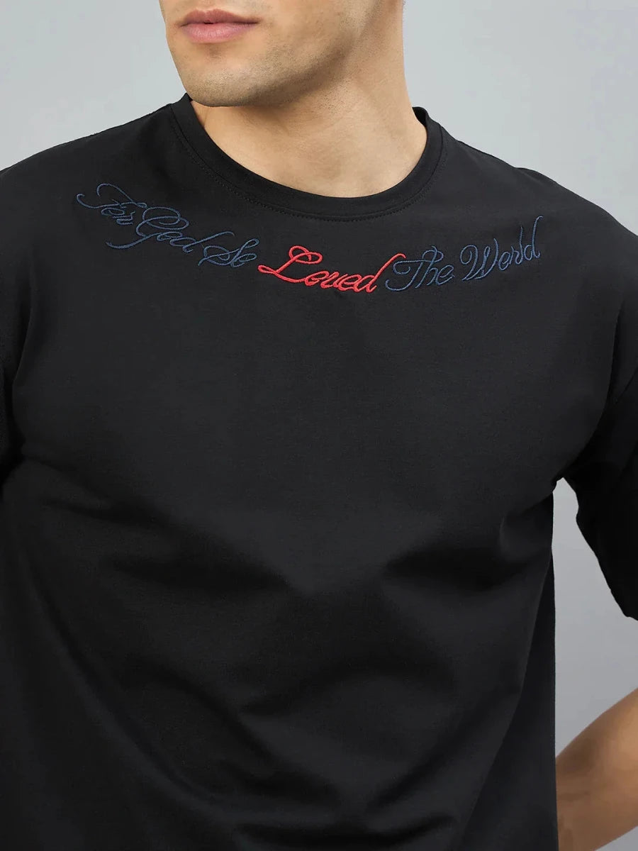 Man in 98degreenorth black oversized tee with Gothic cross embroidery and script on chest.