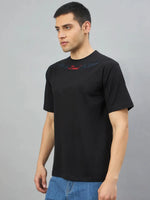 Man in 98degreenorth's Black Graphic Oversized T-Shirt with Gothic Cross embroidery, against a grey background.