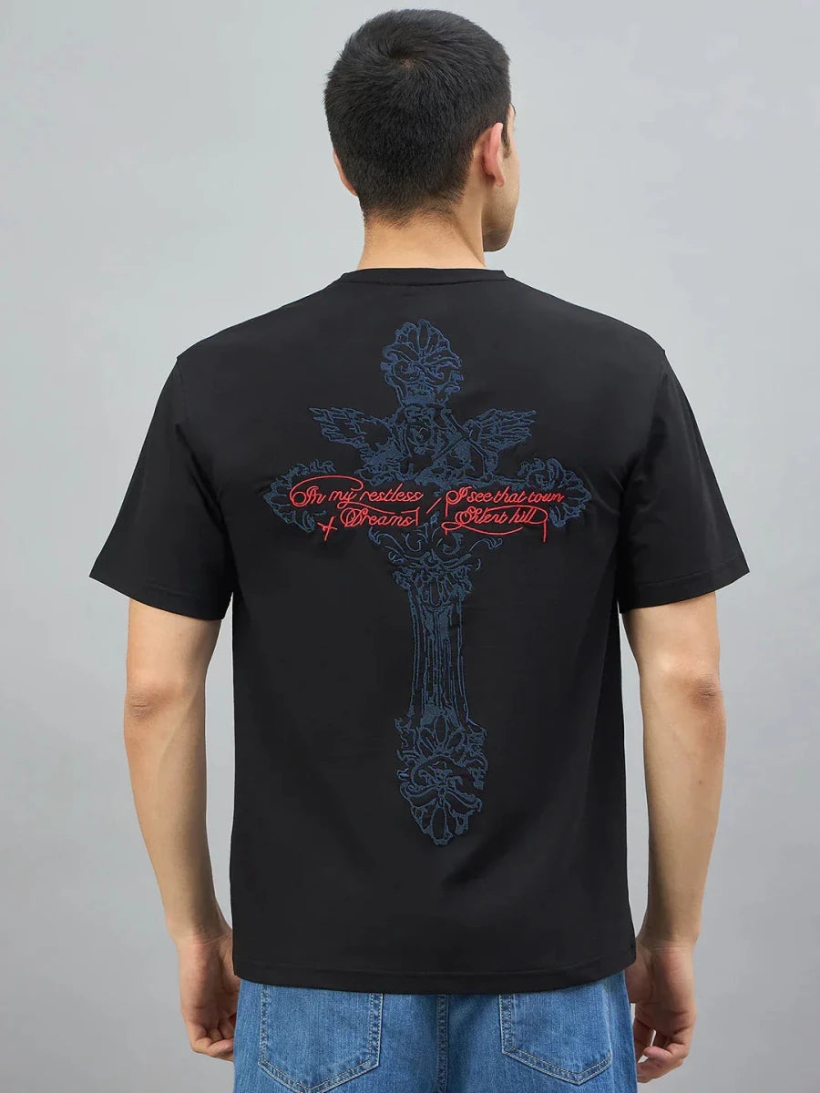 Model wearing 98degreenorth Men's Black Graphic Oversized T-Shirt with large blue cross & red script on back.