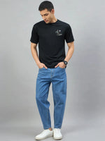 Man wears 98degreenorth's Black Graphic Oversized T-Shirt—RockStar Back Print, blue jeans, and white sneakers.