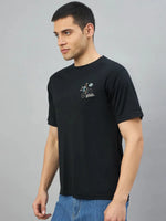 Man wearing 98degreenorth's black oversized graphic t-shirt with RockStar back print, standing sideways on grey background.