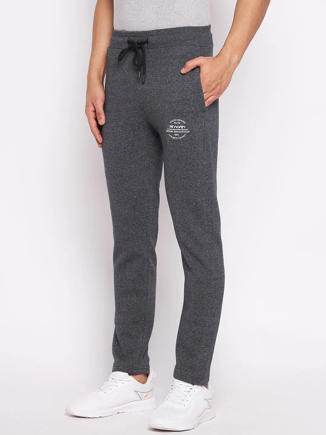 Man wears 98degreenorth Men’s Black Jaspe Fleece Trackpants with drawstring waist and white sneakers against a white backdrop.