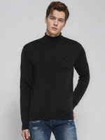 Young man wears 98degreenorth’s Men’s Black Merino Wool Turtle Neck Sweater with blue jeans against a light gray background.