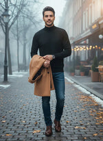 A man in a 98degreenorth Black Merino Wool Turtle Neck Sweater walks on a foggy street, holding a tan coat.