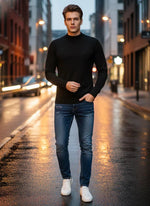 A man wears a 98degreenorth Men’s Black Merino Wool Turtle Neck Sweater with jeans on a wet city street at dusk.