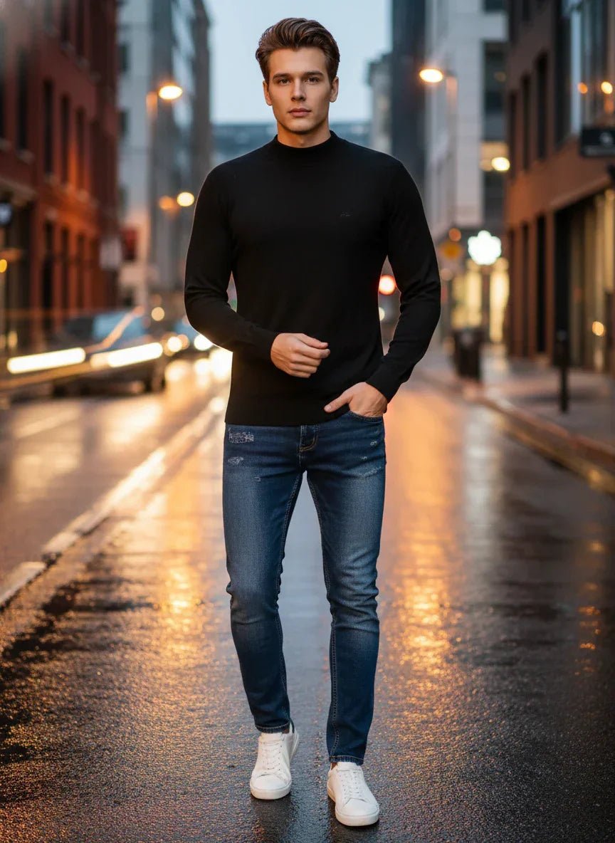 A man wears a 98degreenorth Men’s Black Merino Wool Turtle Neck Sweater with jeans on a wet city street at dusk.