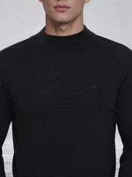 A man wearing a 98degreenorth Men’s Black Merino Wool Turtle Neck Sweater with a subtle chest logo.