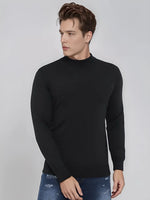 A man wears a 98degreenorth Men’s Black Merino Wool Turtle Neck Sweater and blue jeans against a light gray background.