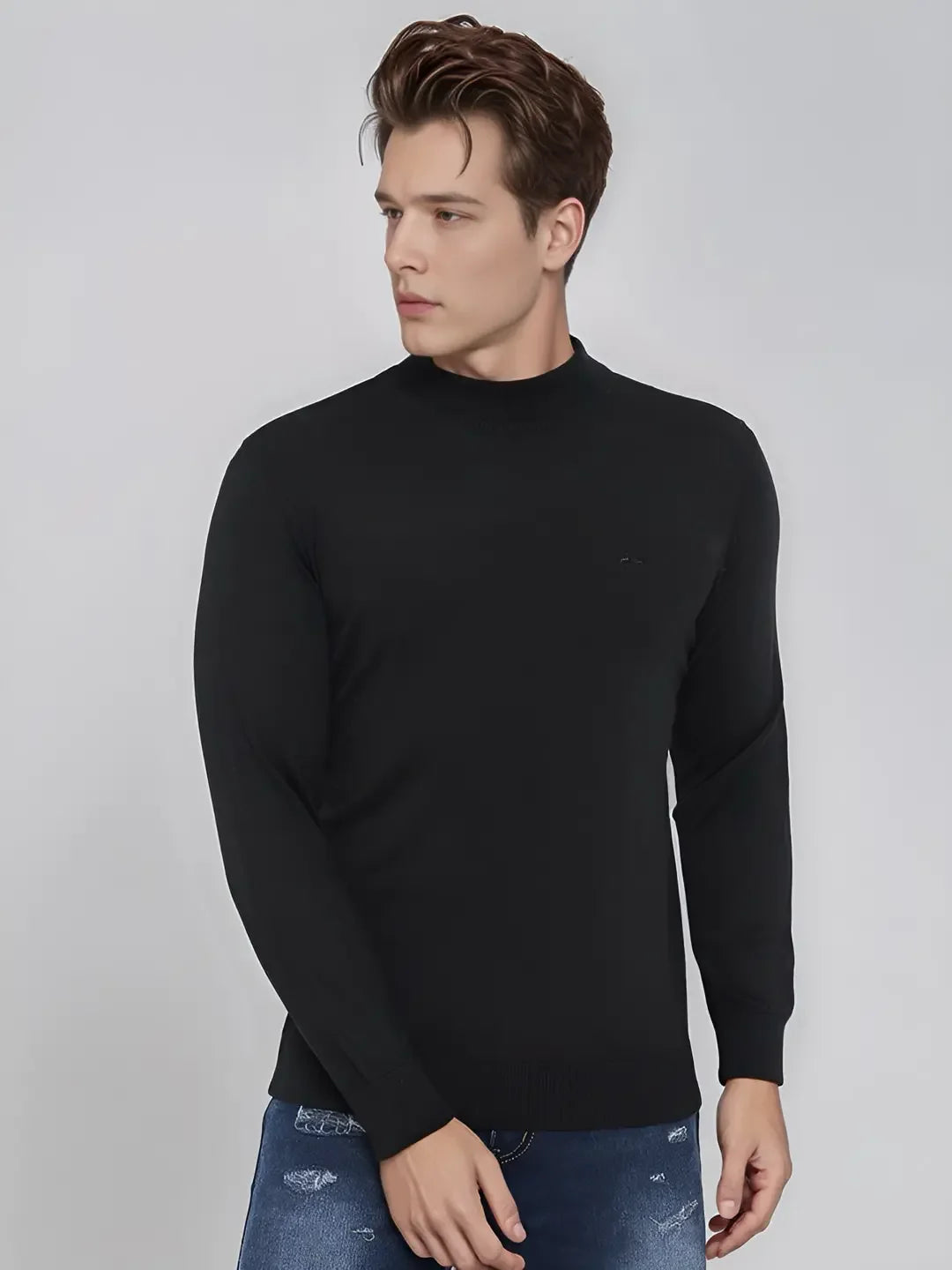 A man wears a 98degreenorth Men’s Black Merino Wool Turtle Neck Sweater and blue jeans against a light gray background.