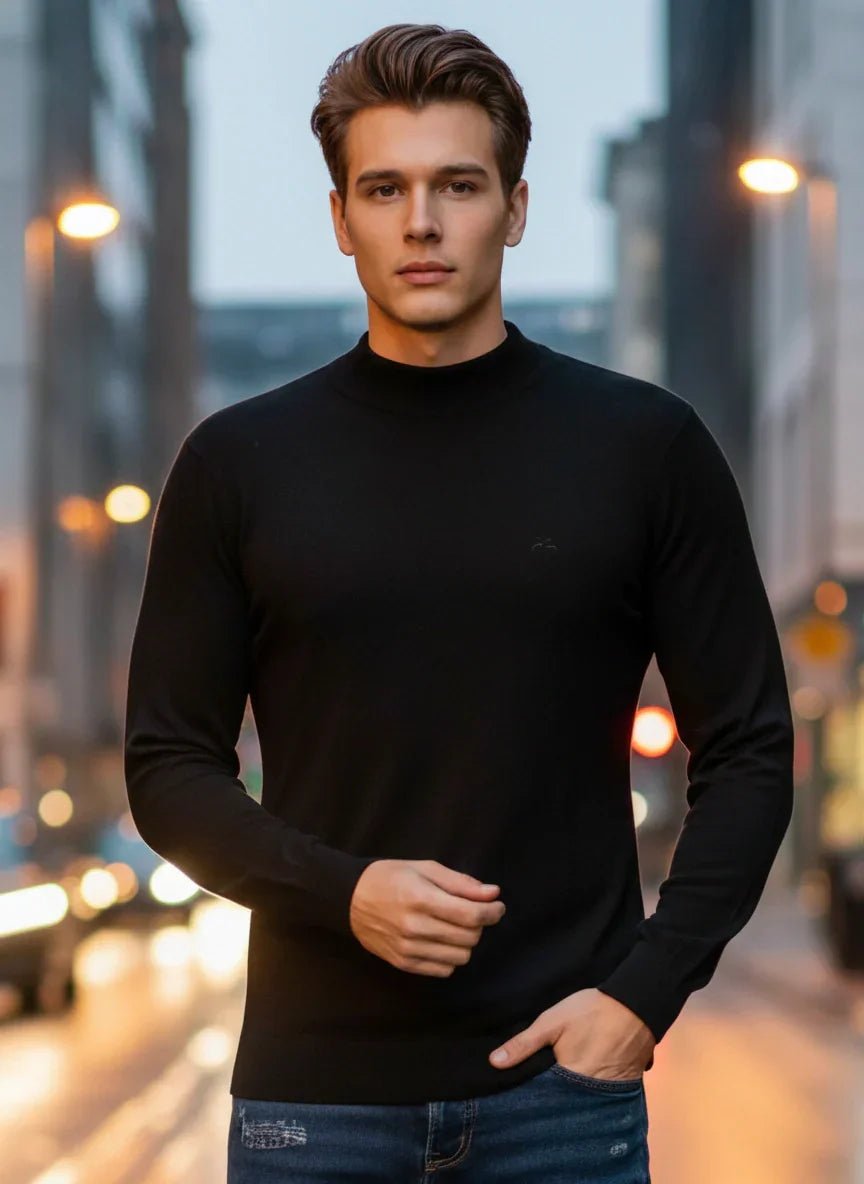 A man wears a 98degreenorth Men’s Black Merino Wool Turtle Neck Sweater on a city street at dusk with blurred lights behind.