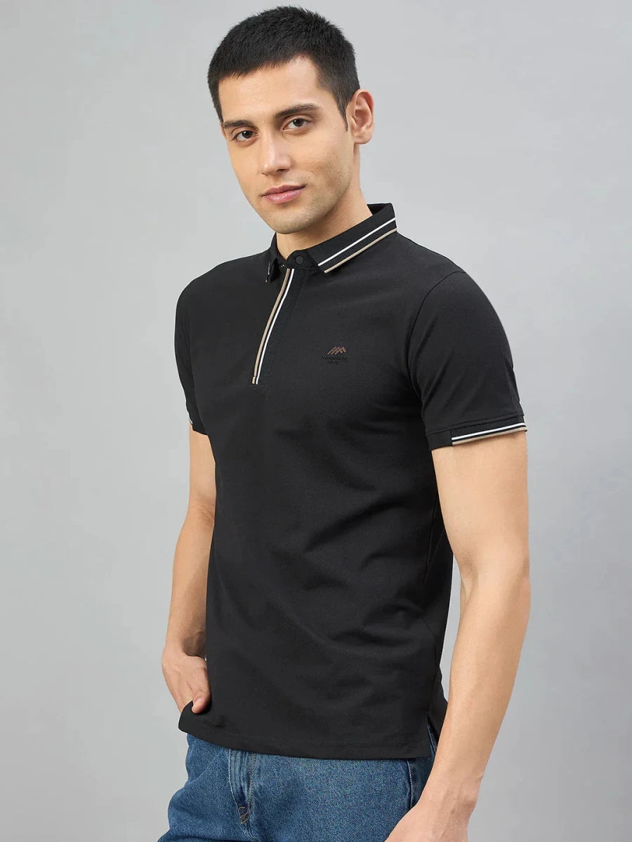 Man in 98degreenorth Men's Black Polo T-Shirt—Handmade Series with Contrast Tipping, hand in pocket on grey backdrop.