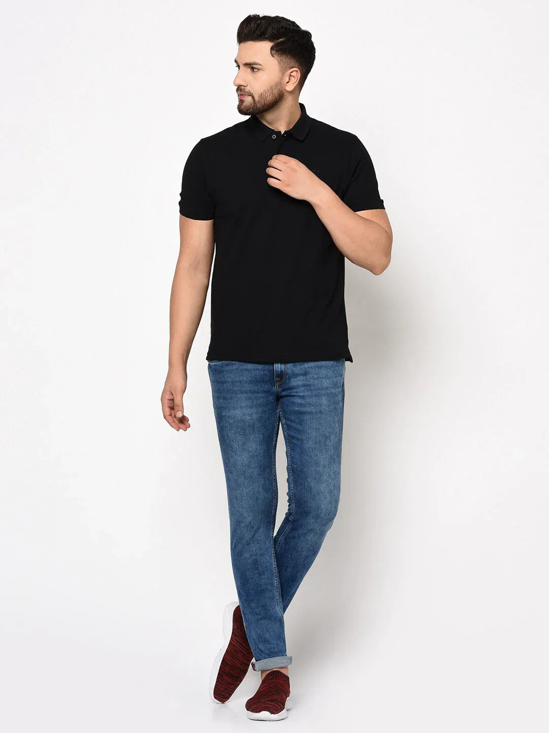 Man wears 98degreenorth Men's Black Polo T-Shirt in stretch cotton pique, blue jeans, and red shoes, looking sideways.