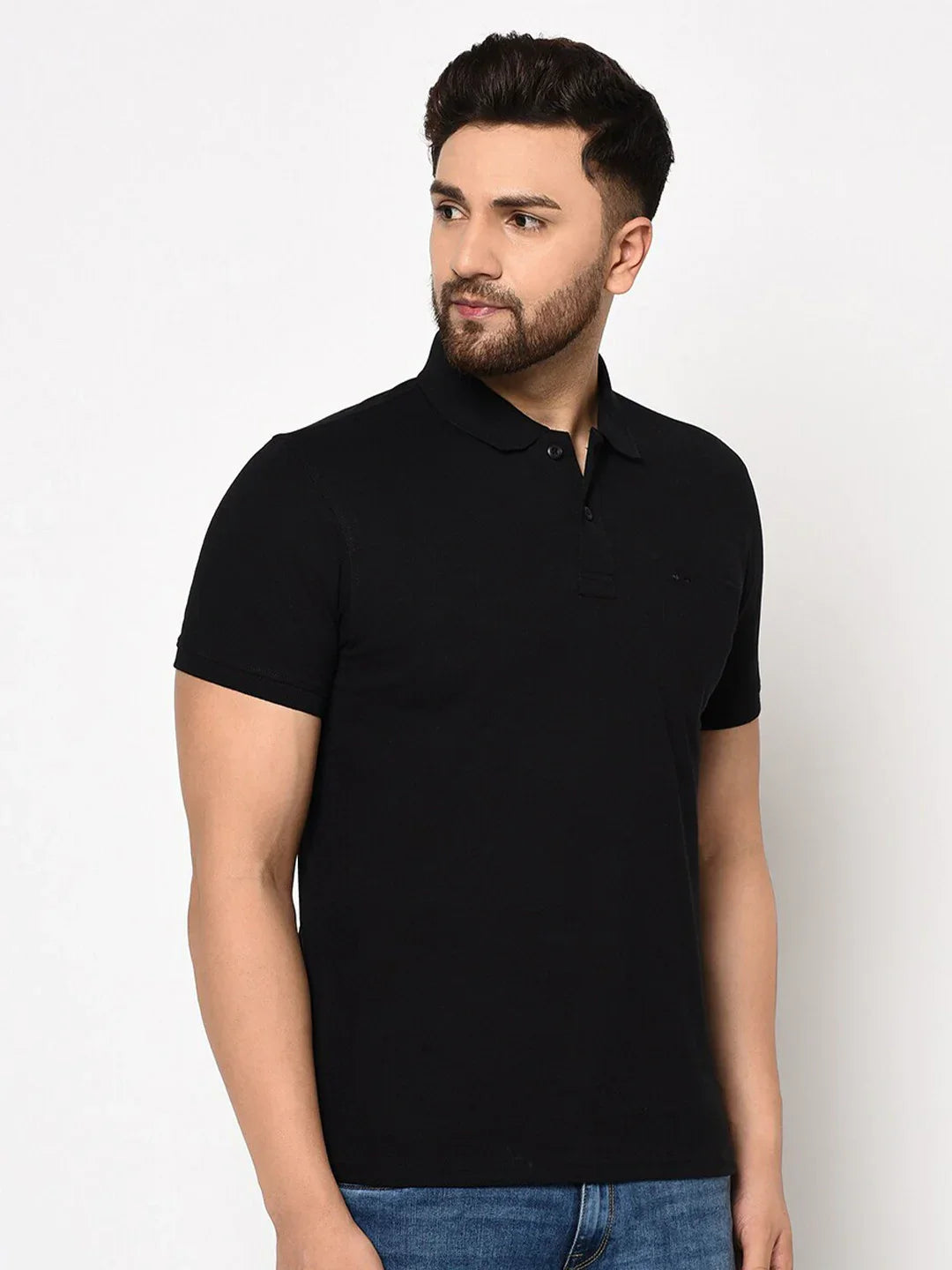 Man wears 98degreenorth Black Stretch Cotton Pique Polo with chest pocket and blue jeans; stands against plain background.