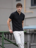 A man in a Men's Black Quarter Zip Polo T-Shirt by 98degreenorth leans on a green railing outdoors, facing the camera.
