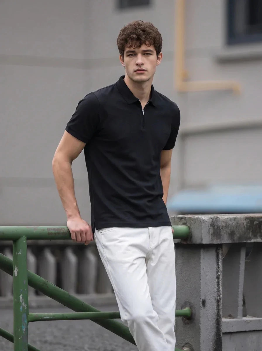 A man in a Men's Black Quarter Zip Polo T-Shirt by 98degreenorth leans on a green railing outdoors, facing the camera.