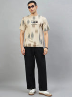 Man in 98degreenorth Camel Abstract Ikat Print T-Shirt, black pants, white sneakers stands against gray background.