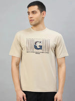Man in 98degreenorth Men's Camel Graphic Oversized T-Shirt with Varsity G print, against a plain gray background.