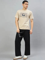 Man in 98degreenorth Men's Camel Graphic Oversized T-Shirt, black pants, white sneakers, holding sunglasses.