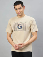 Man wearing 98degreenorth Men's Camel Graphic Oversized T-Shirt with Varsity G print, against a gray background.