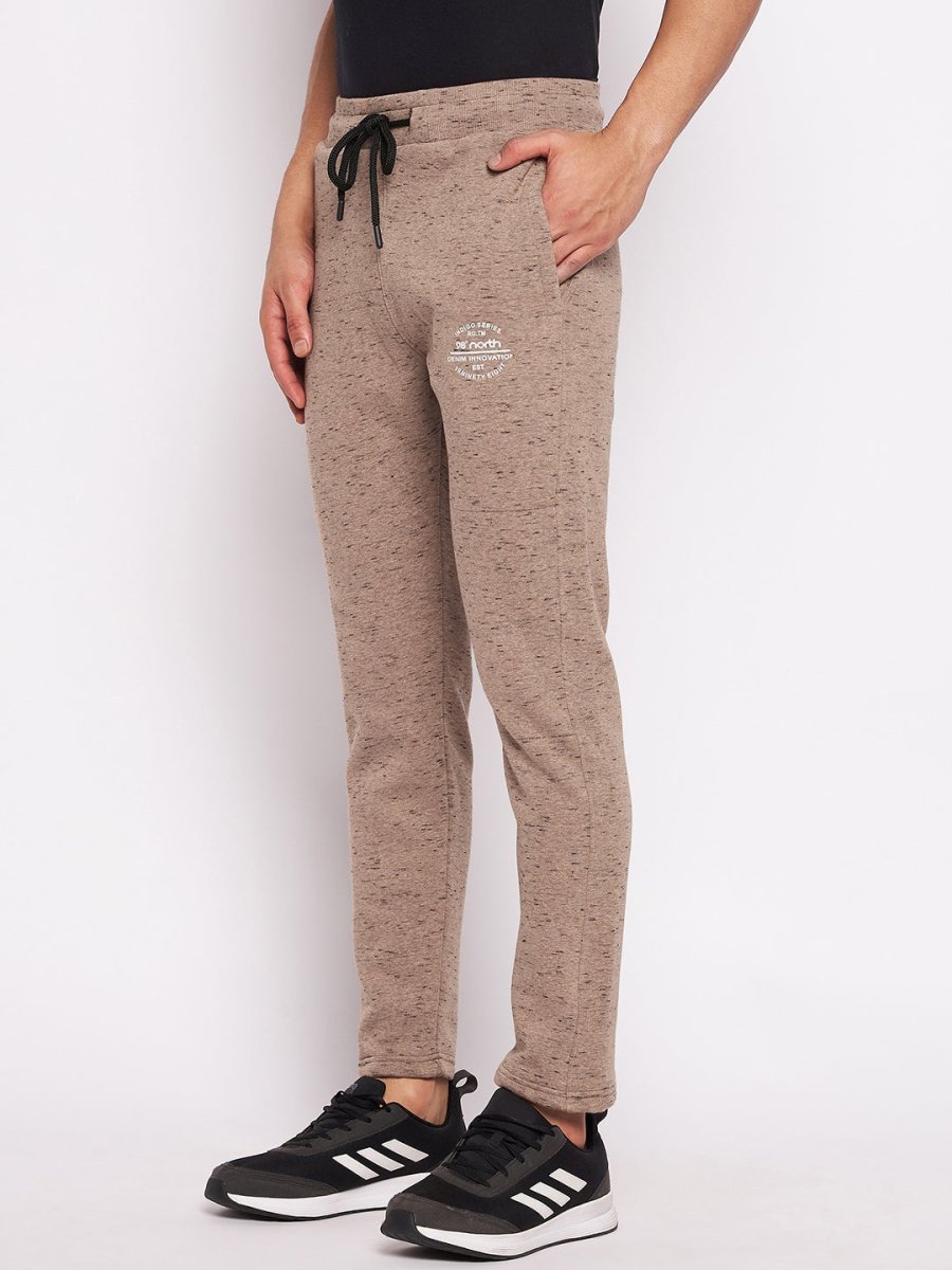 Man wears 98degreenorth Men’s Camel Melange Fleece Trackpants with a black tee and Adidas sneakers against a white background.