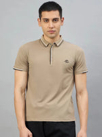 A man wears the 98degreenorth Men's Camel Polo T-Shirt — Handmade Series, standing against a gray background.