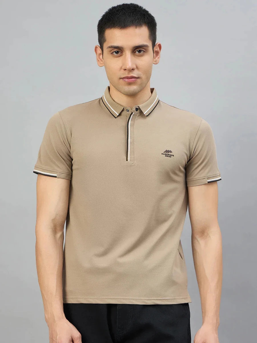 A man wears the 98degreenorth Men's Camel Polo T-Shirt — Handmade Series, standing against a gray background.