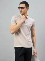 Man in 98degreenorth Men's Camel Polo T-Shirt with White Tipping, styled with black pants on a gray background.