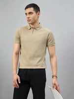 Man in a 98degreenorth Men's Camel Quarter Zip Polo T-Shirt, black pants, stands with a white chair against gray.