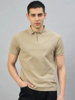A man wears the 98degreenorth Men's Camel Quarter Zip Polo T-Shirt—Popcorn Knit, with black pants, on a gray background.