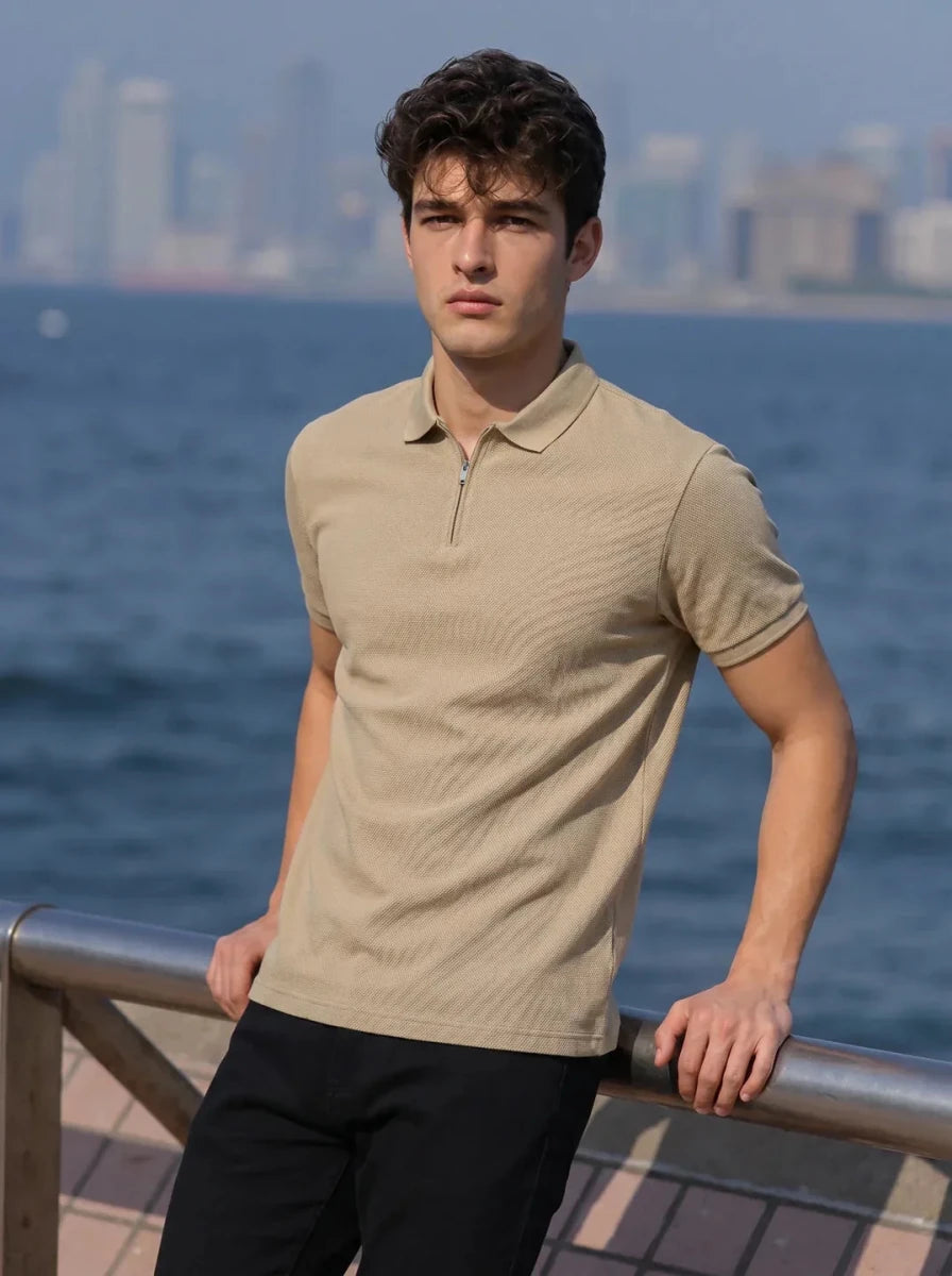 A young man in the 98degreenorth Men’s Camel Quarter Zip Polo stands by a waterfront with a city skyline behind him.