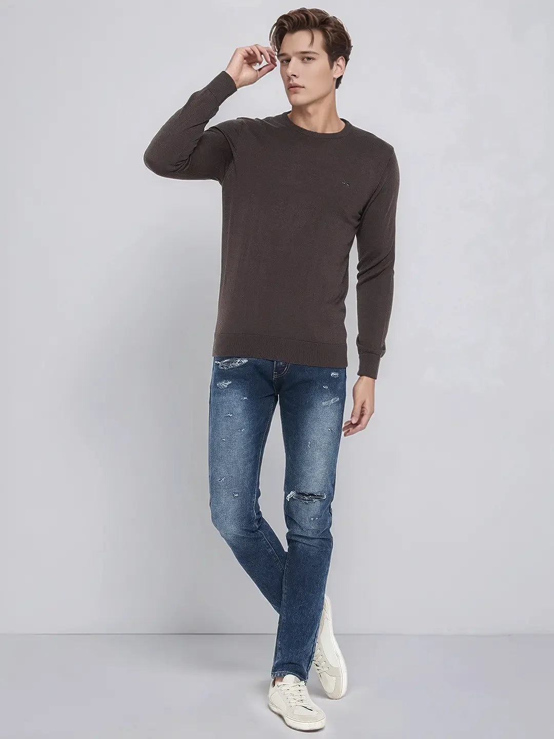Man in a 98degreenorth Men’s Charcoal Merino Wool Round Neck Sweater, blue jeans, and sneakers on a light gray background.