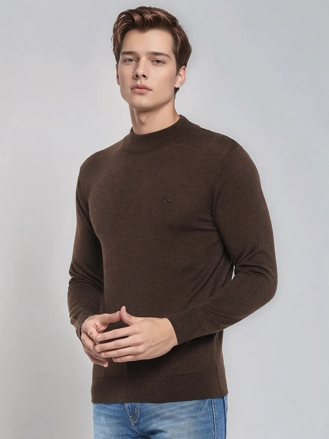 A man wears the 98degreenorth Coffee Merino Wool Turtle Neck Sweater with blue jeans against a light gray background.