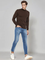 Man wears 98degreenorth Coffee Merino Wool Turtle Neck Sweater with blue jeans and white sneakers against gray background.