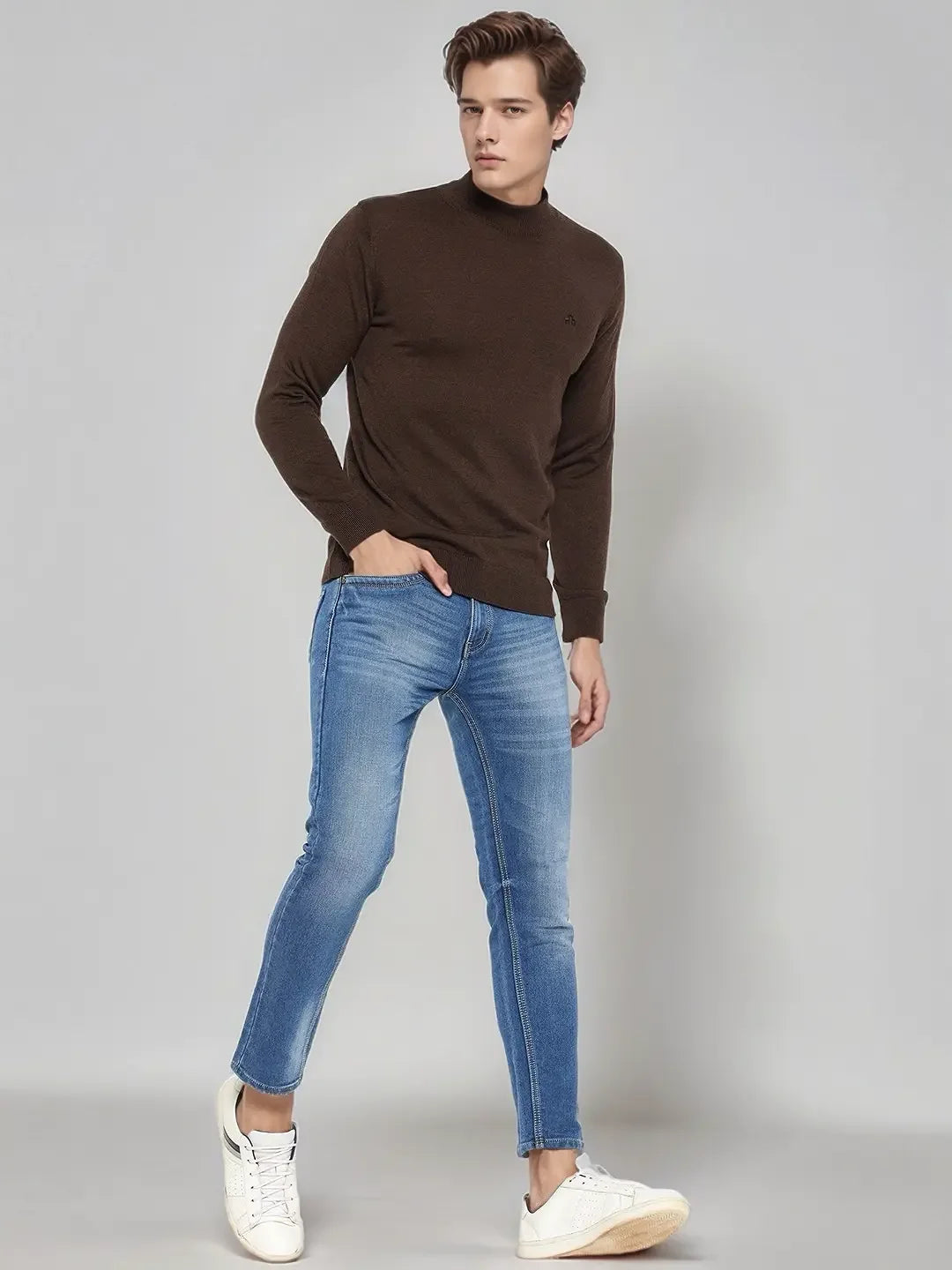 Man wears 98degreenorth Coffee Merino Wool Turtle Neck Sweater with blue jeans and white sneakers against gray background.