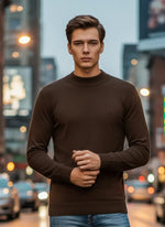 A man wears the 98degreenorth Men’s Coffee Merino Wool Turtle Neck Sweater on a city street at dusk with blurred lights.