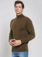 A man wears a 98degreenorth Men’s Coffee Merino Wool Turtle Neck Sweater and blue jeans against a light gray background.