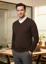 A man in a 98degreenorth Men’s Coffee Merino Wool V-Neck stands in a modern office with desk, laptop, and books.