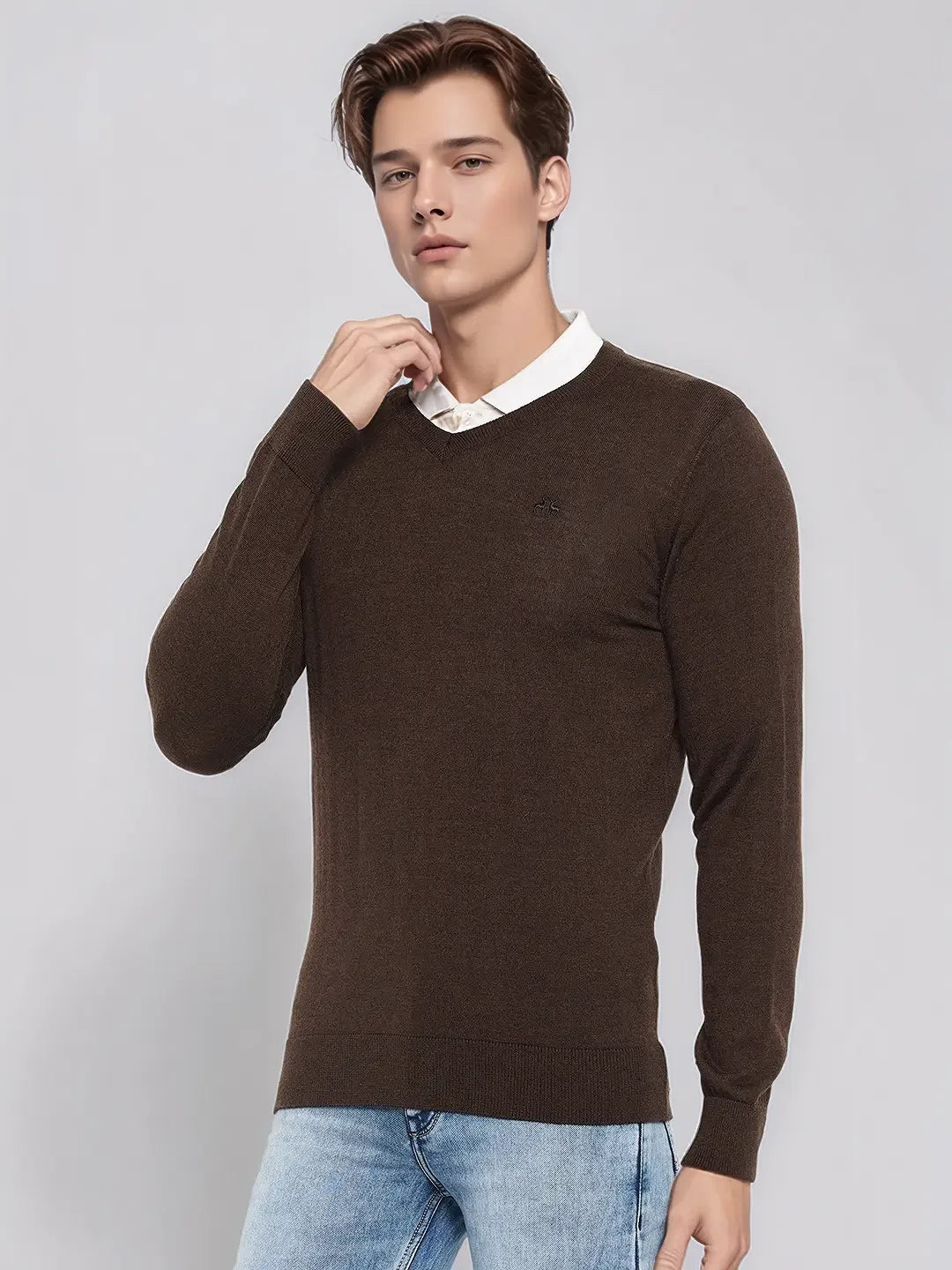 A man wears the 98degreenorth Men’s Coffee Merino Wool V-Neck Sweater over a white shirt with light blue jeans.