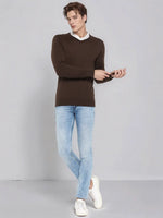 Man wears 98degreenorth Men’s Coffee Merino Wool V-Neck Sweater, light blue jeans, and white sneakers on a gray backdrop.