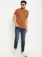 Man wears 98degreenorth Men's Copper Polo T-Shirt, blue jeans, white sneakers & sunglasses against white background.