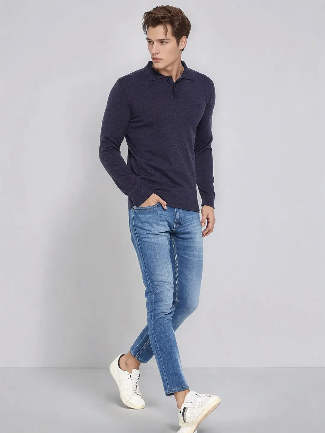 A man in 98degreenorth’s Men’s Dark Denim Merino Wool Polo Neck Sweater walks against a gray background.