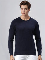 A man wears a 98degreenorth Dark Denim Merino Wool Round Neck Sweater with white pants against a light gray background.