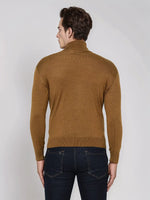 Man wears 98degreenorth Men’s Dark Khaki Merino Wool Turtle Neck Sweater with dark jeans against a plain background.