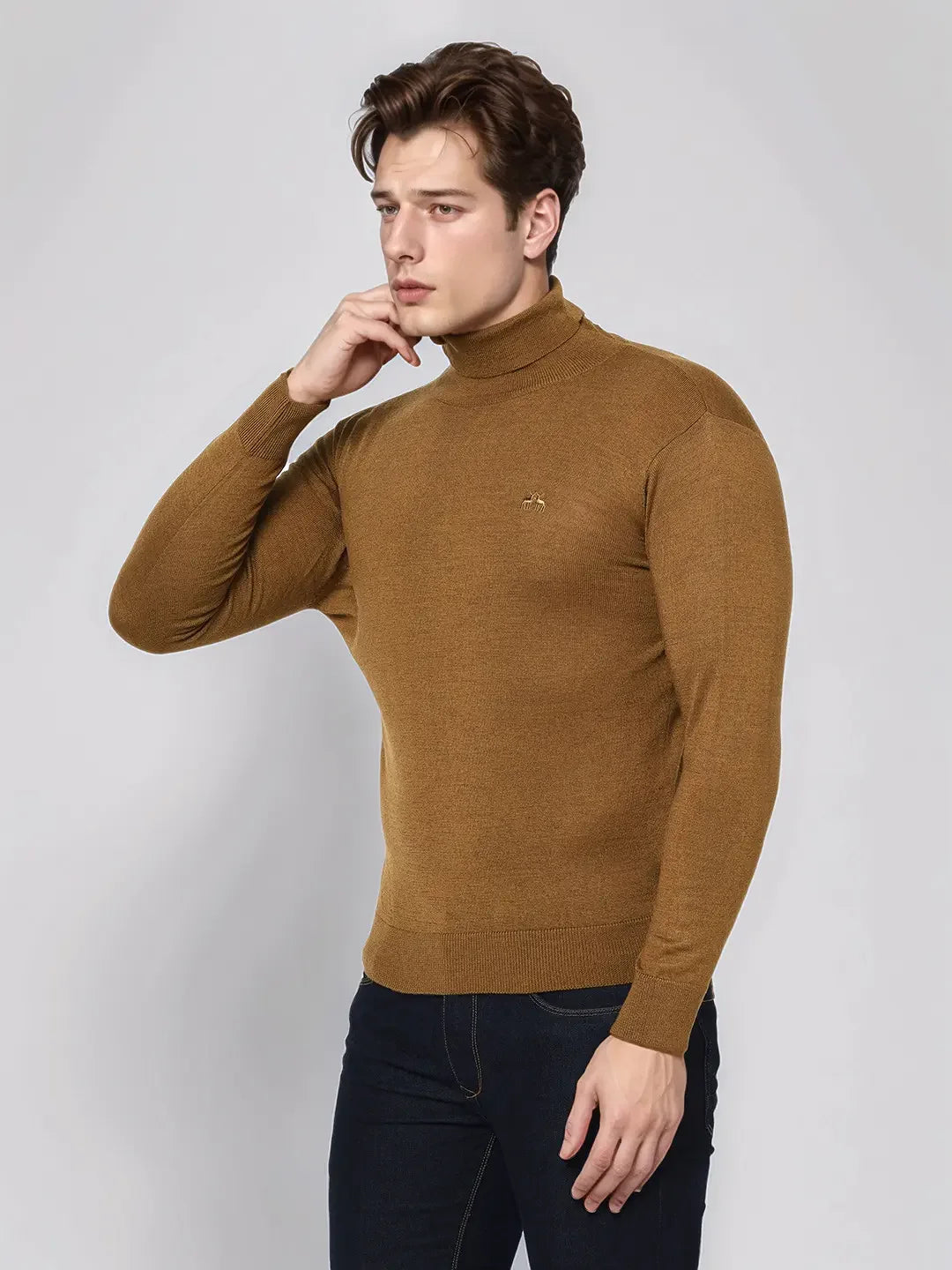 Man in a 98degreenorth Dark Khaki Merino Wool Turtle Neck Sweater and dark jeans stands against a light background.